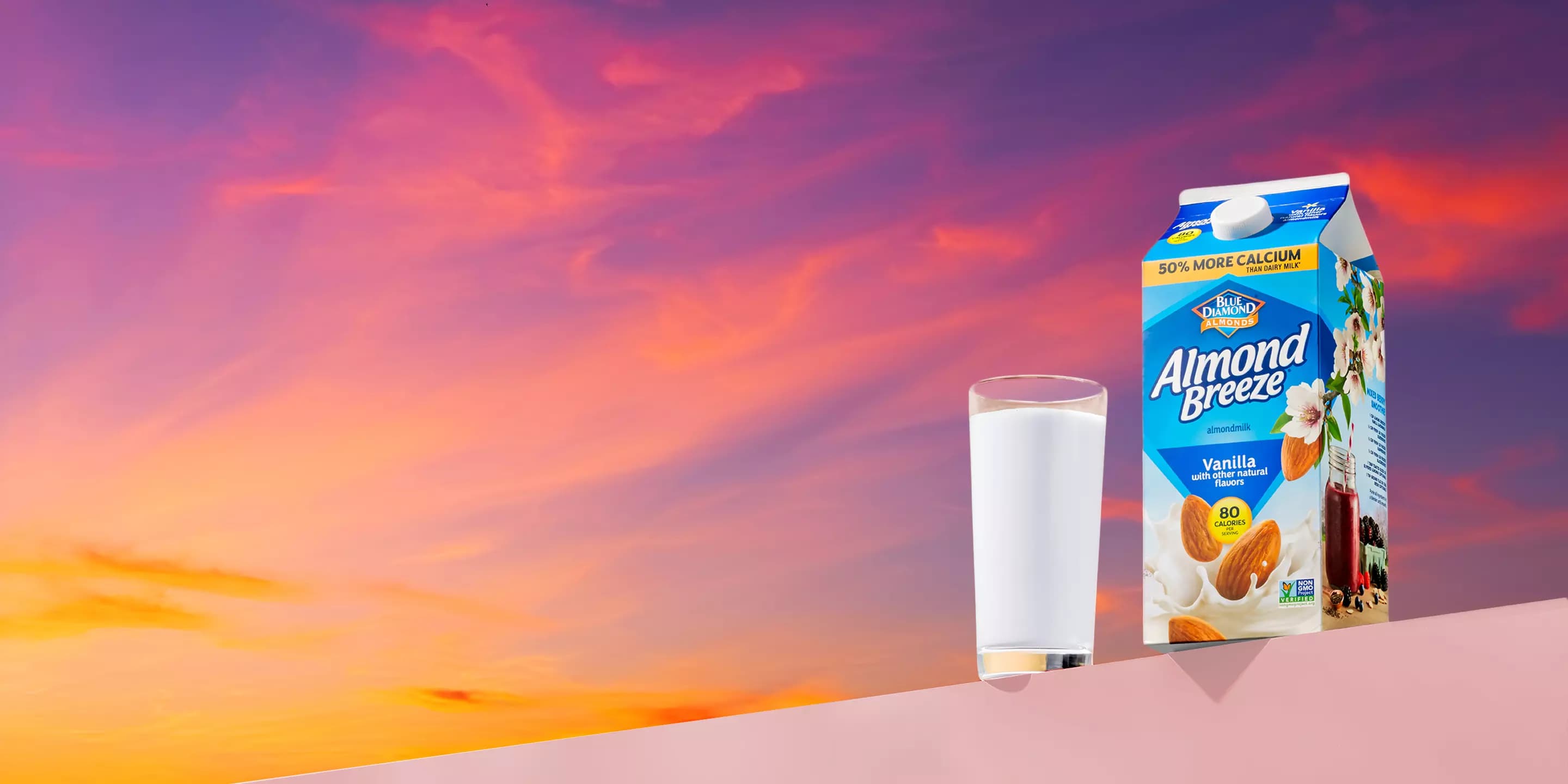 Glass and carton of Almond Breeze almond milk with a sunset background