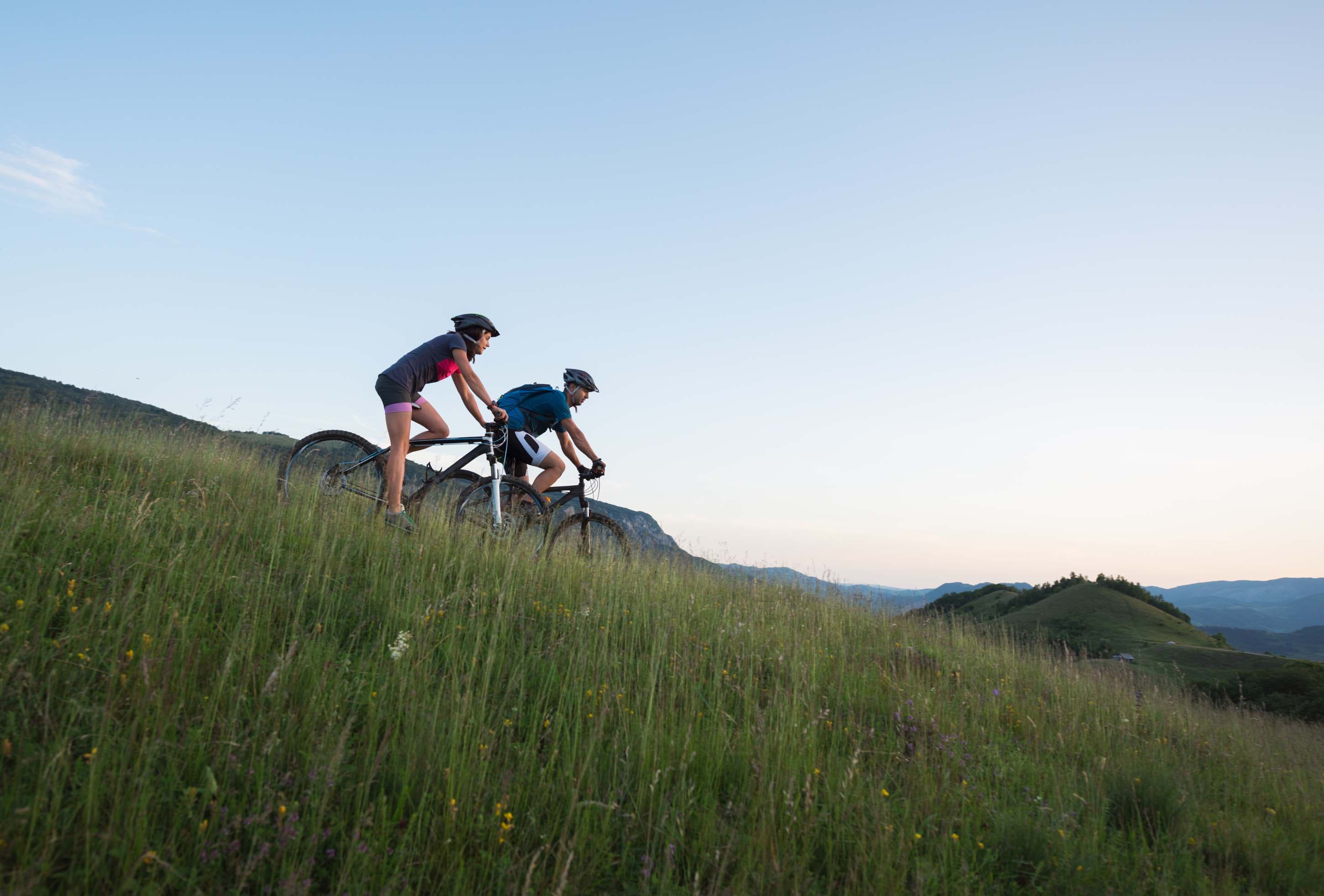 Couple mountain biking down a grassy hill