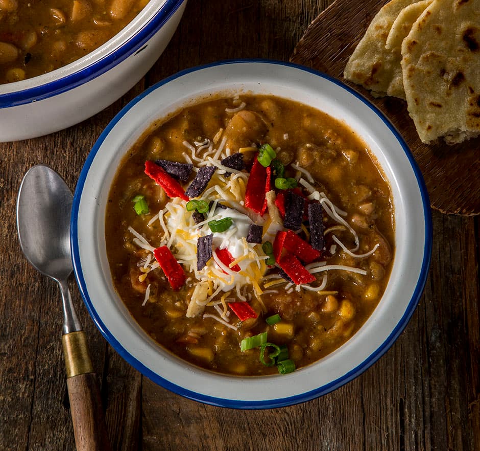 Bowl of vegetarian bean chili topped with shredded cheese and tortilla chips