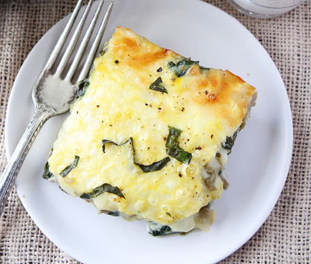 Square piece of spinach artichoke egg casserole on a white plate