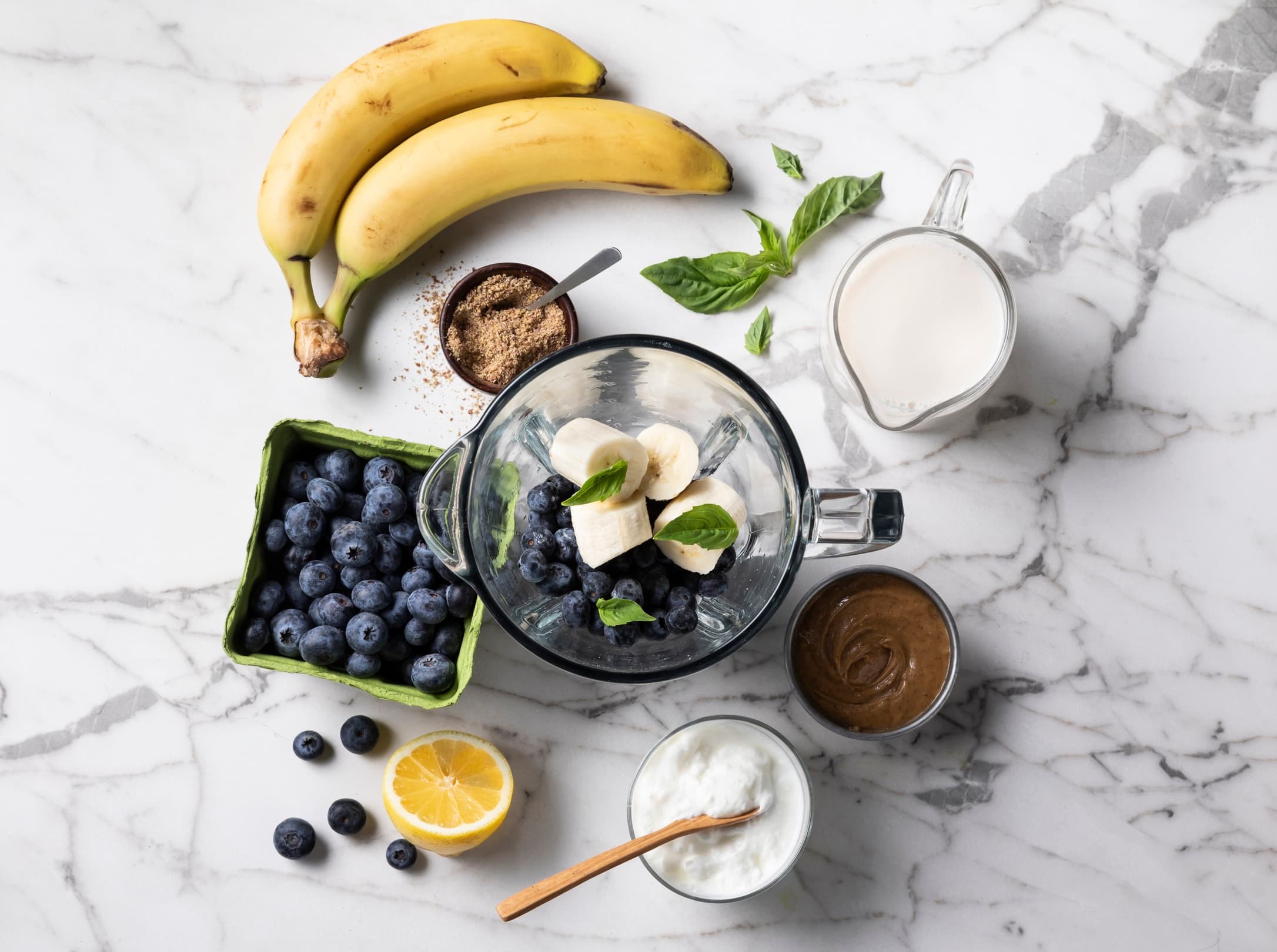 Counter top full of fresh fruit, almondmilk, and a blender full of ingredients