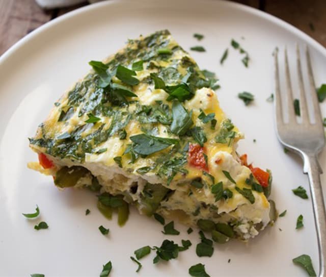 Slice of gluten-free crustless quiche with spring vegetables garnished with fresh parsley