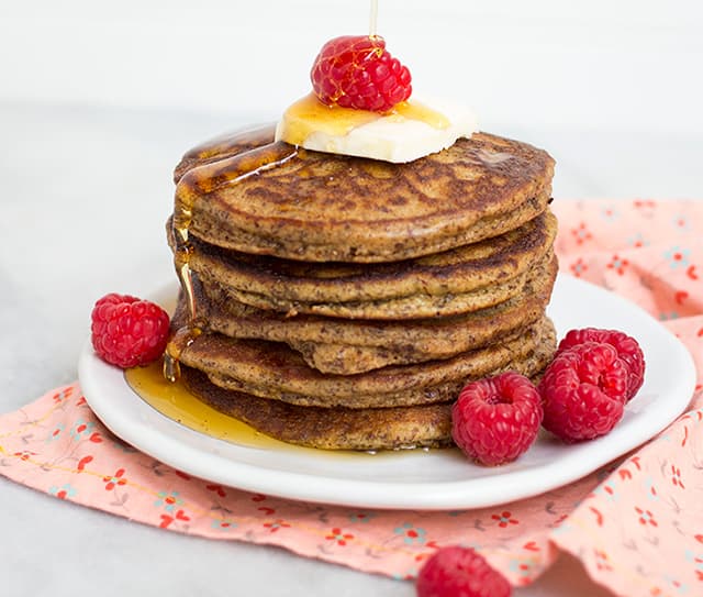 Stack of gluten-free pancakes topped with butter, syrup and fresh raspberries