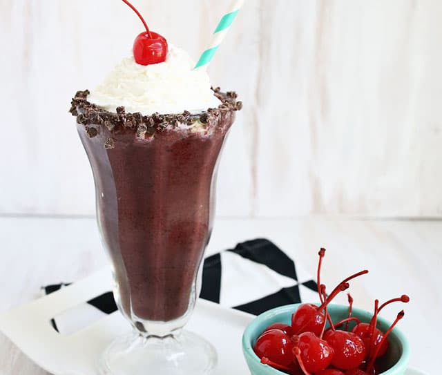 Chocolate covered cherry shake topped with whipped cream and a cherry, with chocolate chunks around the rim