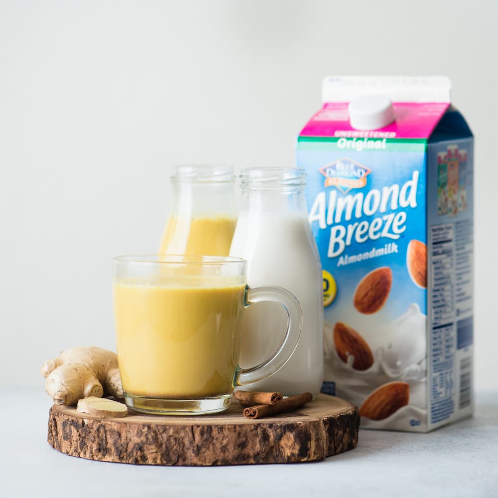 Mug of golden milk latte next to a half gallon of Almond Breeze almondmilk