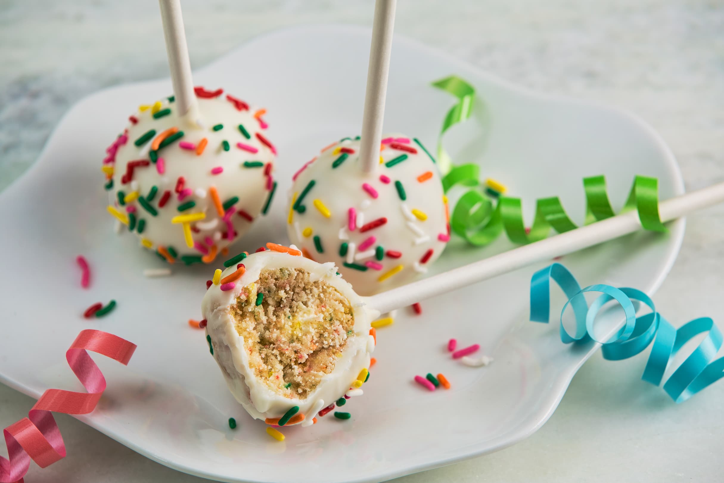 Three decorative breeze birthday cake pops covered in white chocolate and multicolored sprinkles