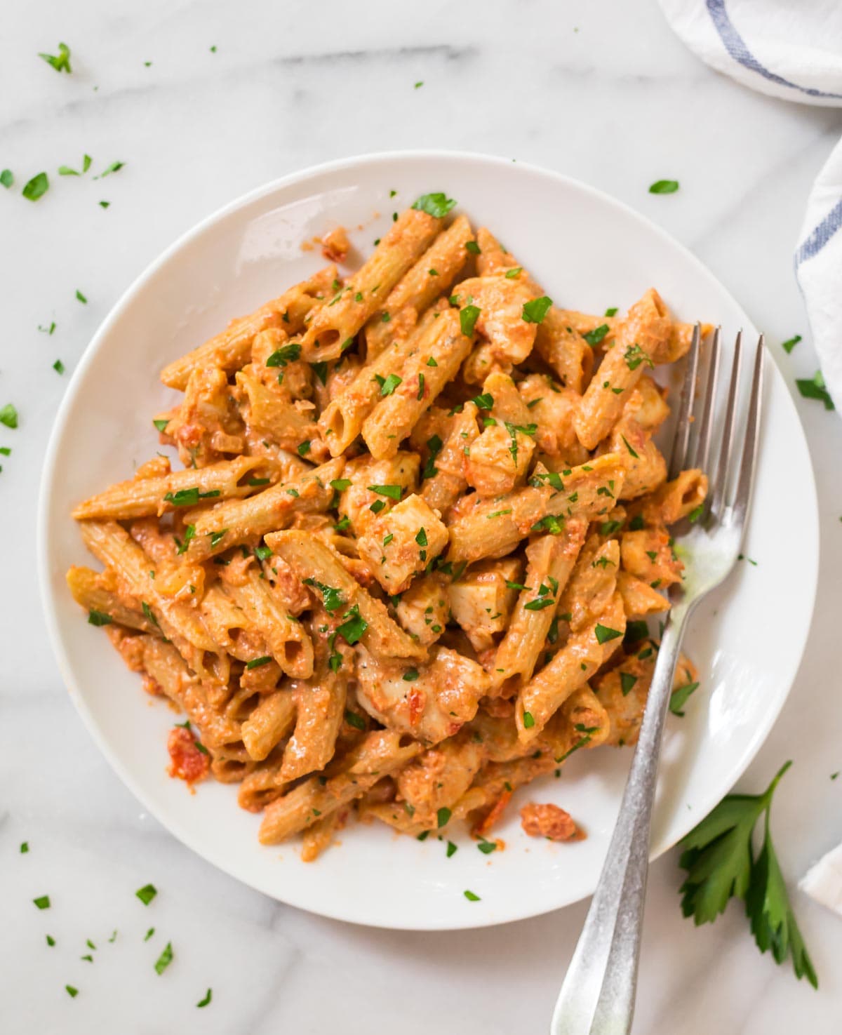 Plate full of penne alla vodka with chicken garnished with parsley