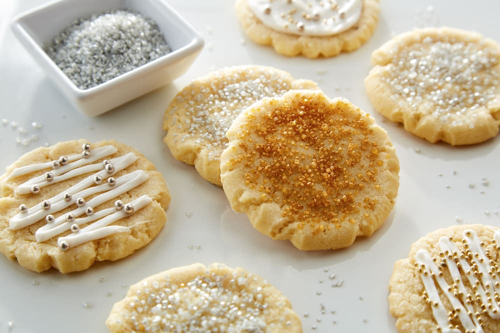Table full of dairy free sugar cookies decorated with silver and gold sprinkles