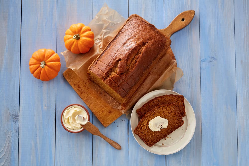 Loaf of pumpkin bread on a cutting board with two slices on a plate