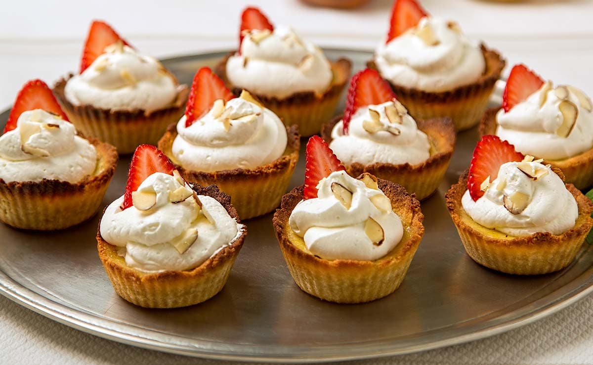 Platter full of gluten-free almond custard tarts topped with whipped cream and almond shavings