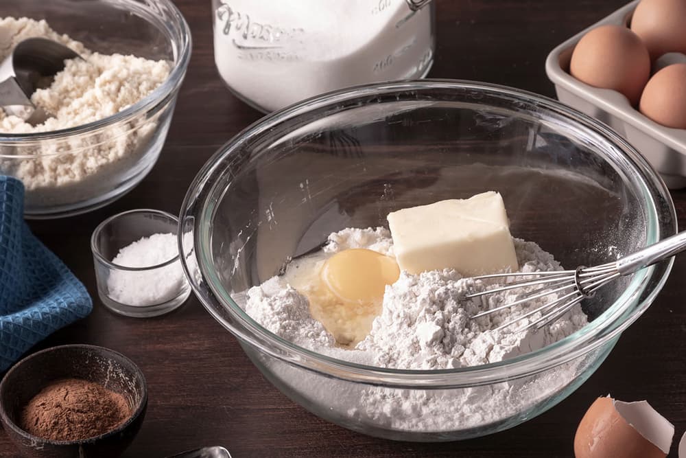 Table top with bowls of flour, butter, eggs, butter and baking utensils