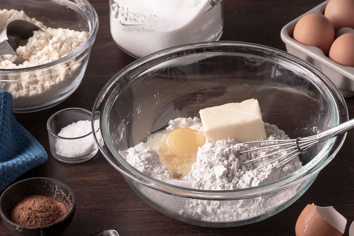 Table top with bowls of flour, butter, eggs, butter and baking utensils