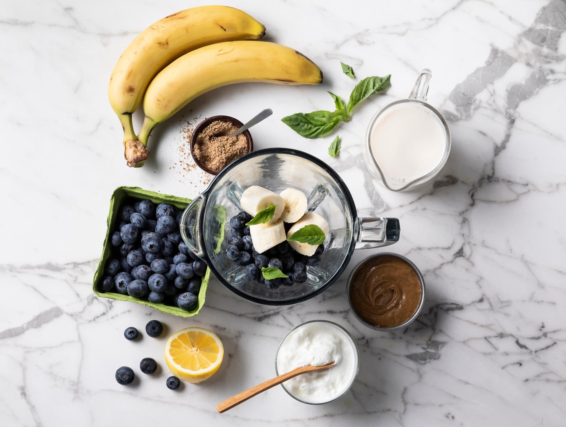 Counter top full of fresh fruit, almondmilk, and a blender full of ingredients