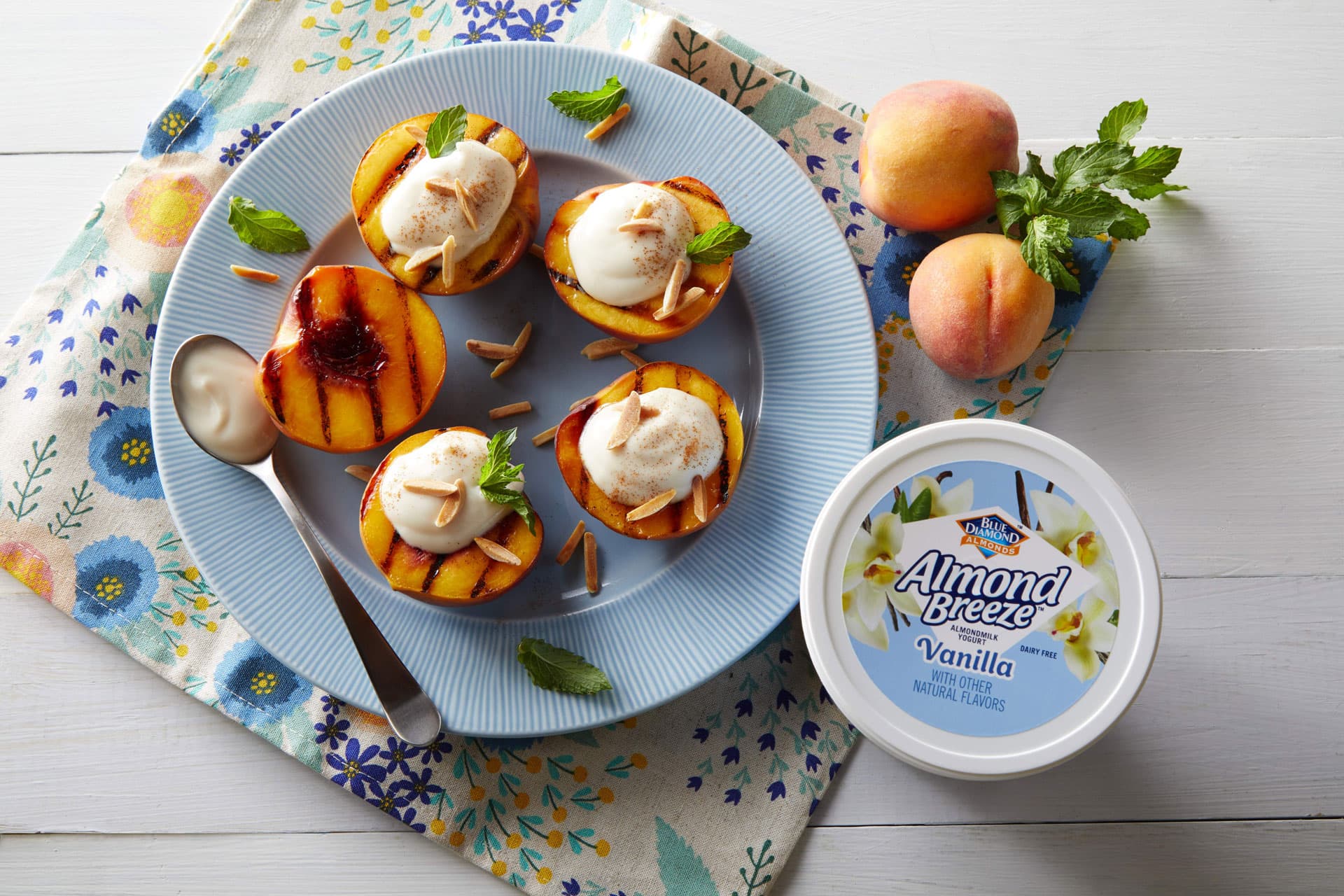 Plate full of grilled peaches topped with Almond Breeze Vanilla Almondmilk Yogurt