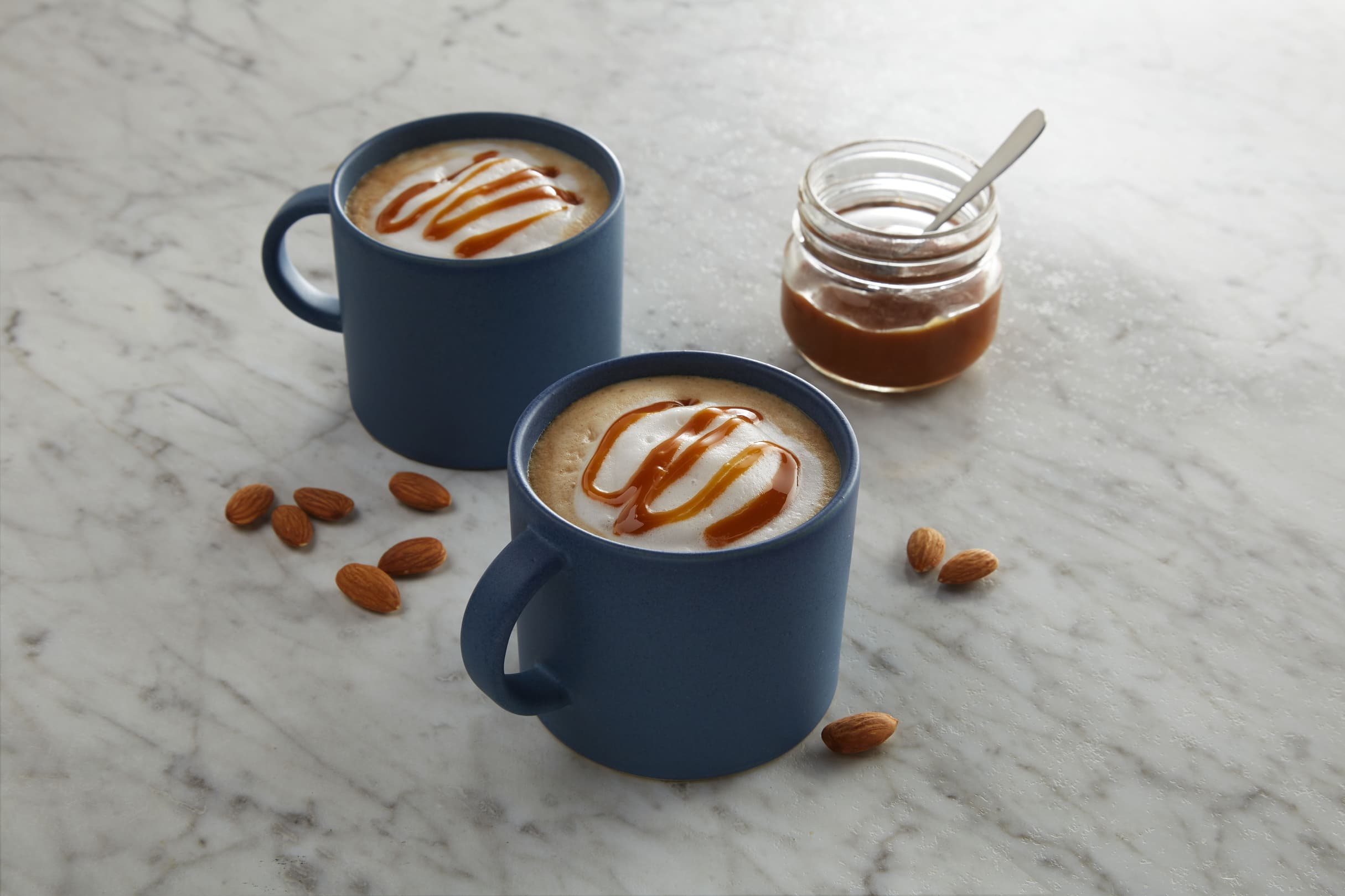 Two dairy-free caramel macchiatos topped with frothed almond milk and caramel sauce