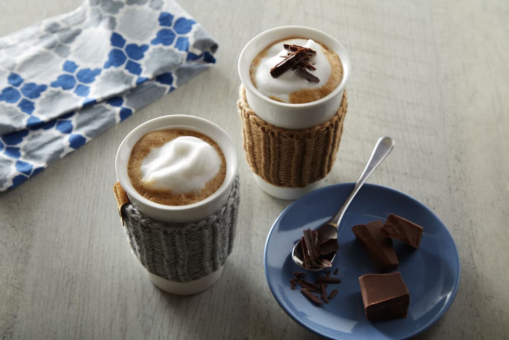 Two dairy-free creamy chocolate mochas next to a plate of chocolate shavings