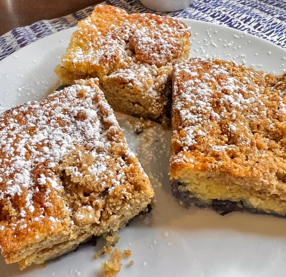 Plate full of almond blueberry coffee cake topped with powdered sugar