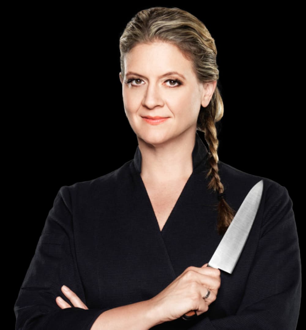 Amanda Freitag wearing a black chefs coat holding a kitchen knife