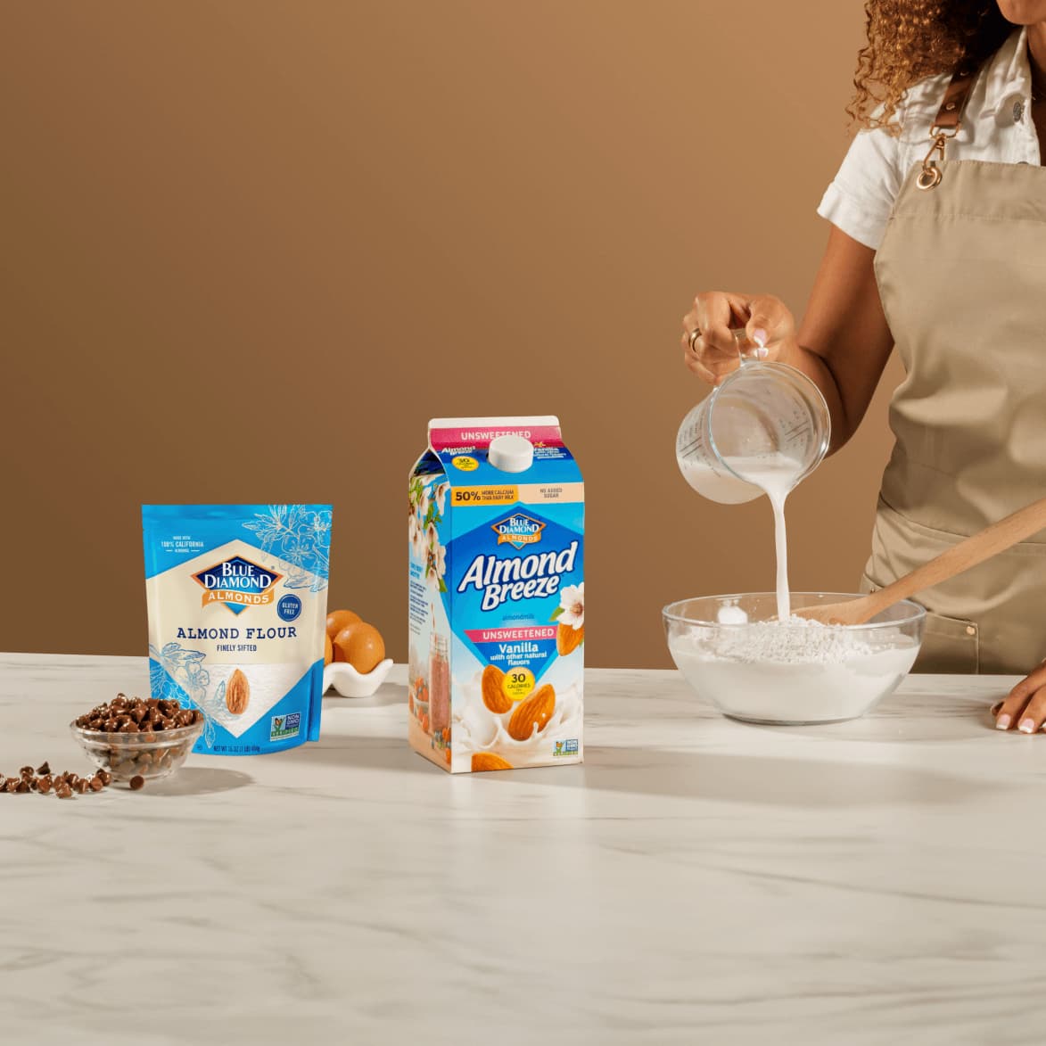 Woman pouring Almond Breeze almondmilk into a bowl of Blue Diamond almond flour.