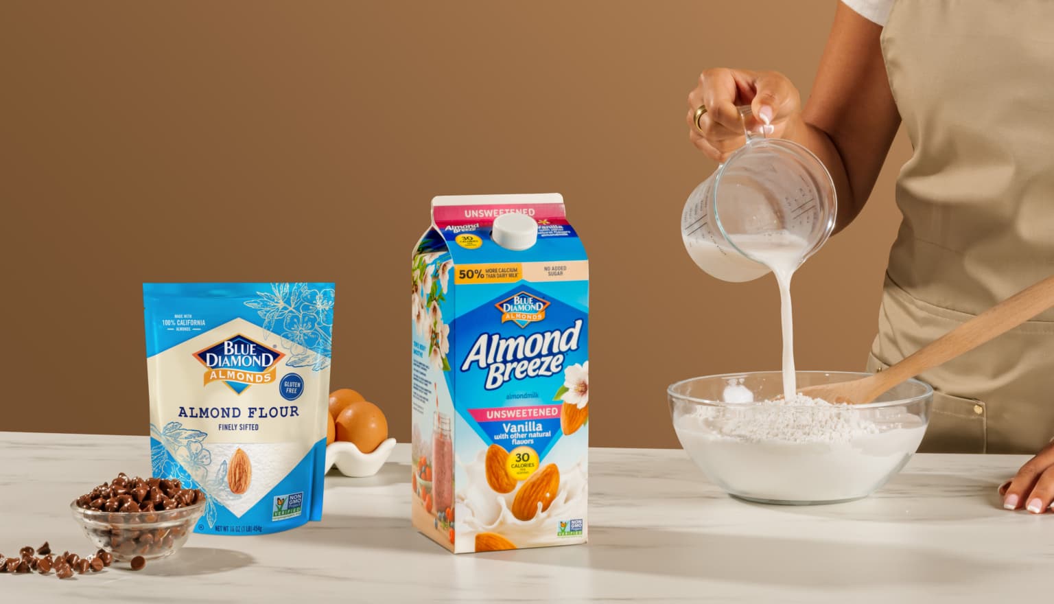 Woman pouring Almond Breeze almondmilk into a bowl of Blue Diamond almond flour.