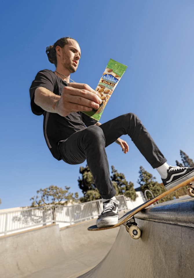 Man skateboarding while holding 1.5oz tube of Bold Wasabi & Soy Sauce almonds.