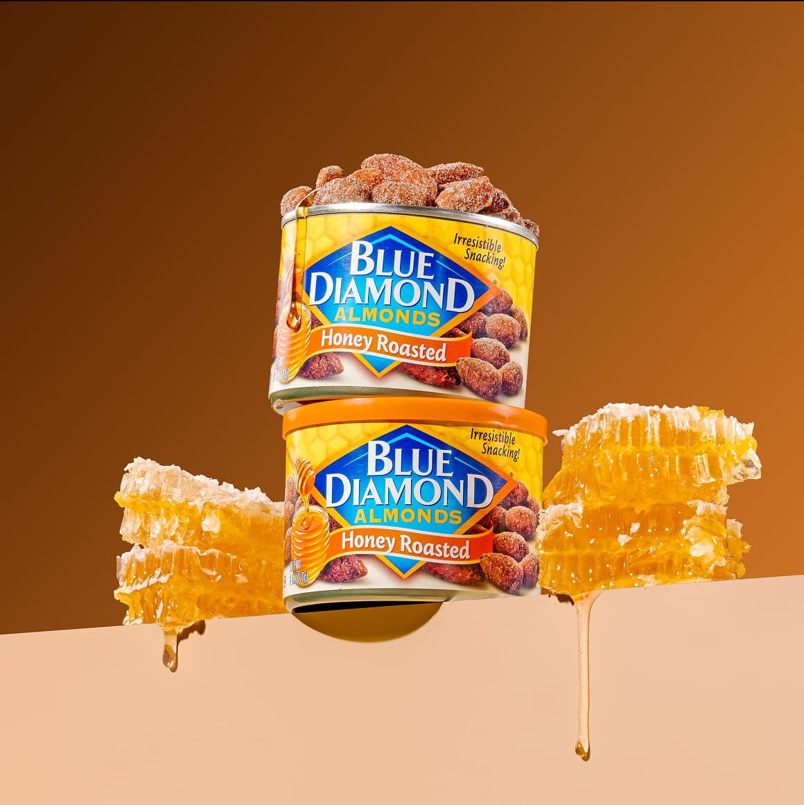 Two cans of Honey Roasted almonds stacked on top of each other. The cans are sitting among some dripping honey comb.