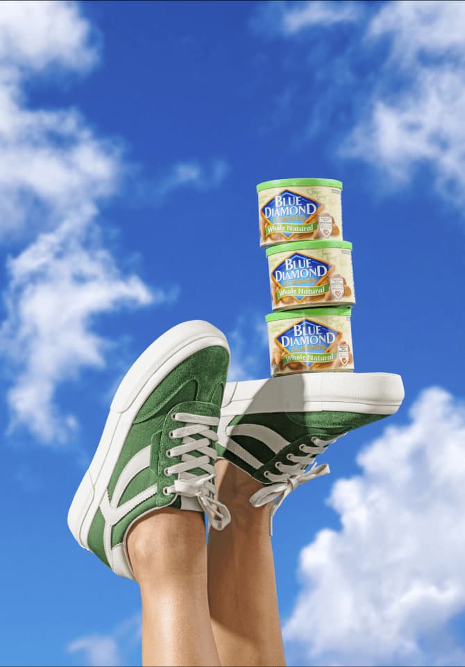 A pair of feet are sticking up into the air with green shoes on. A trio of cans are stacked up on the bottom of the shoes.