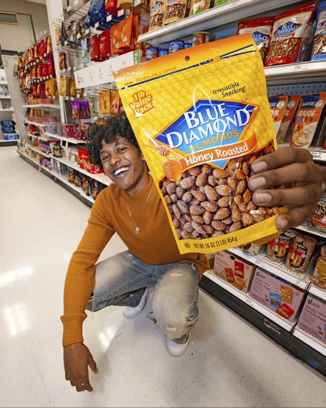 Man in the grocery story isle crouching down while holding a bag of Honey Roasted almonds.