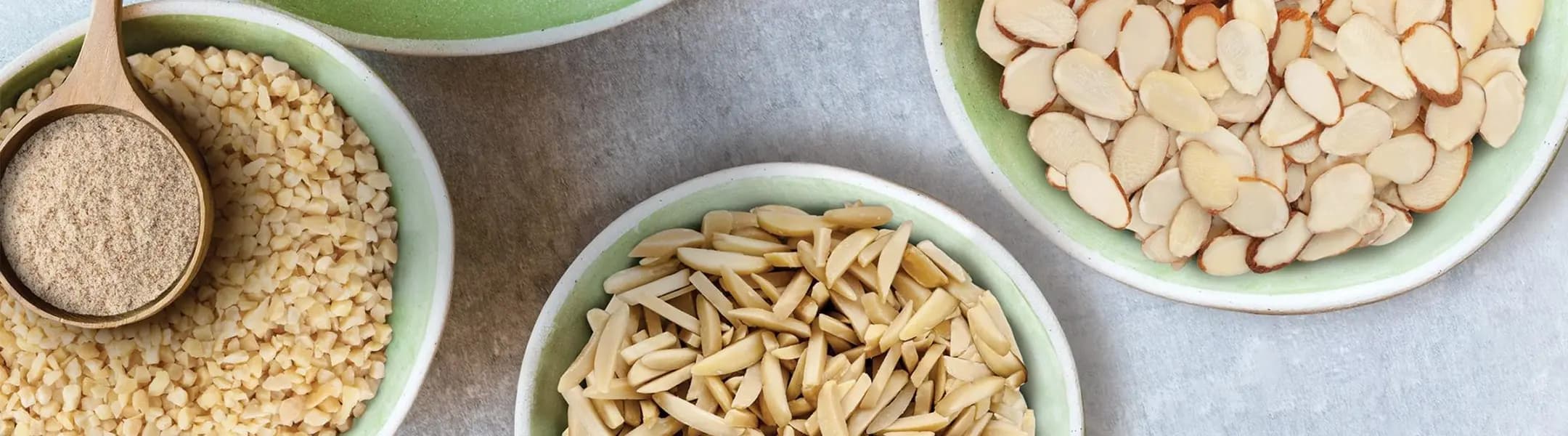 Bowls of sliced, slivered, chopped, and ground almonds arranged on a countertop.