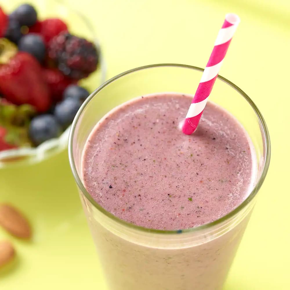 Glass with purple smoothie and straw next to a bowl of fruit