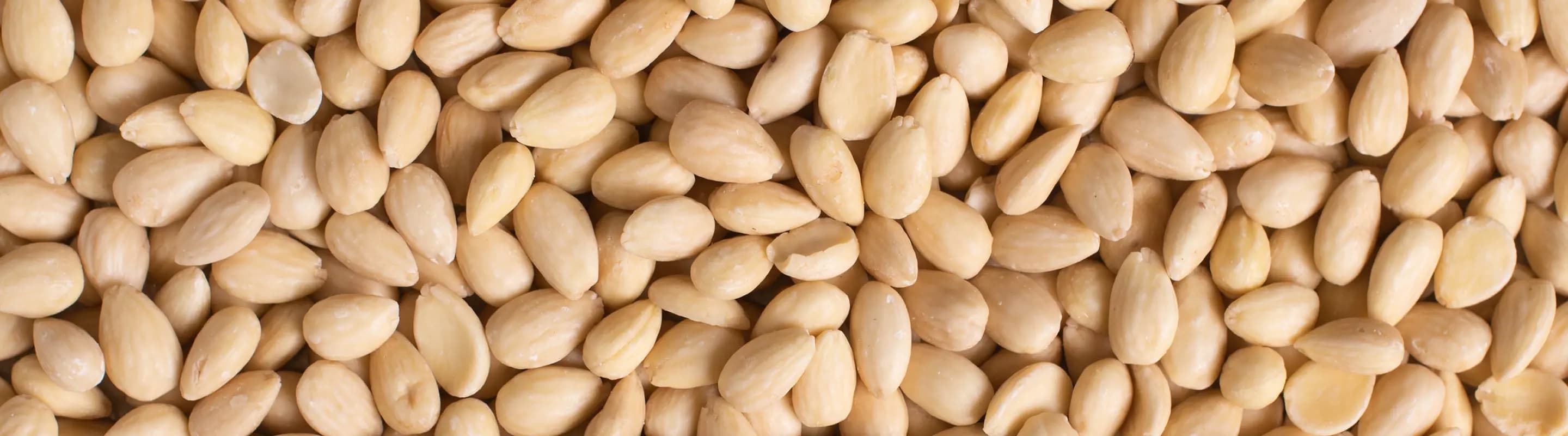Close-up of blanched whole almonds covering the entire frame, creating a seamless background texture.