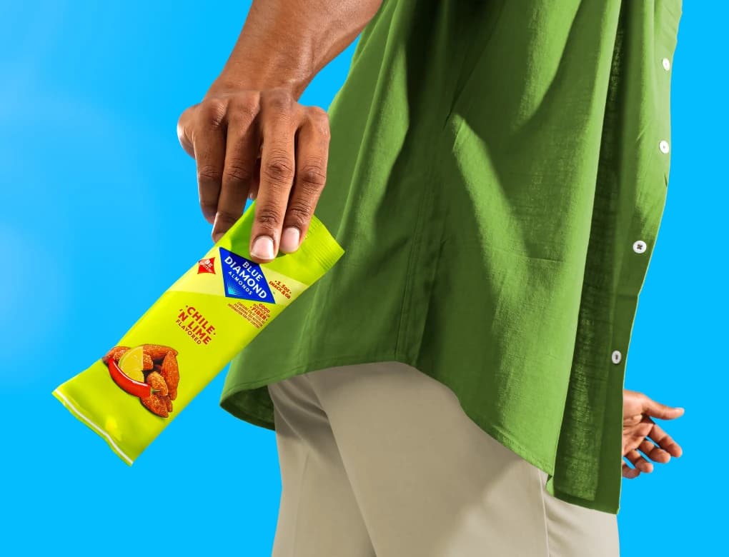 Person holding a Blue Diamond Chile 'n Lime flavored almonds snack pack against a bright blue background.