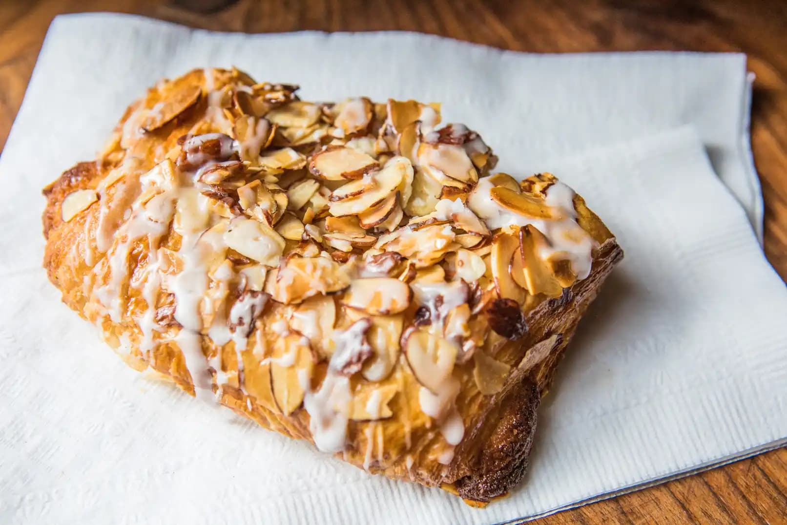 Fresh almond croissant topped with sliced almonds and a sweet glaze, served on a white napkin.
