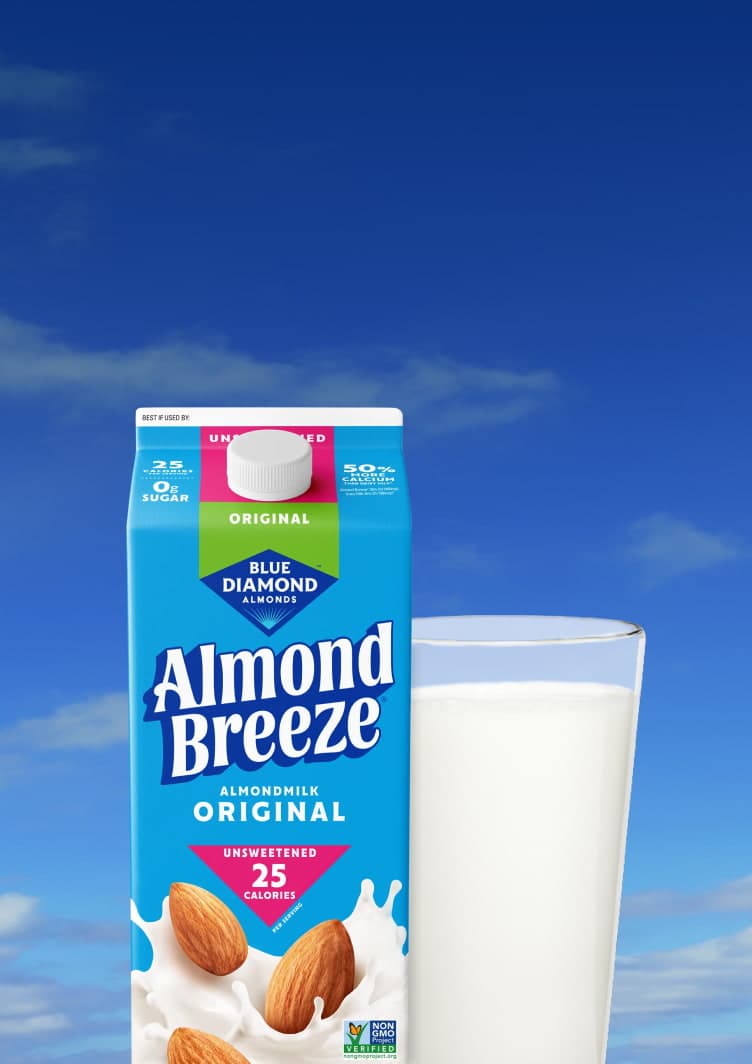 Blue Diamond Almond Breeze Original Unsweetened Almondmilk carton beside a full glass of almondmilk against a bright blue sky with soft white clouds.