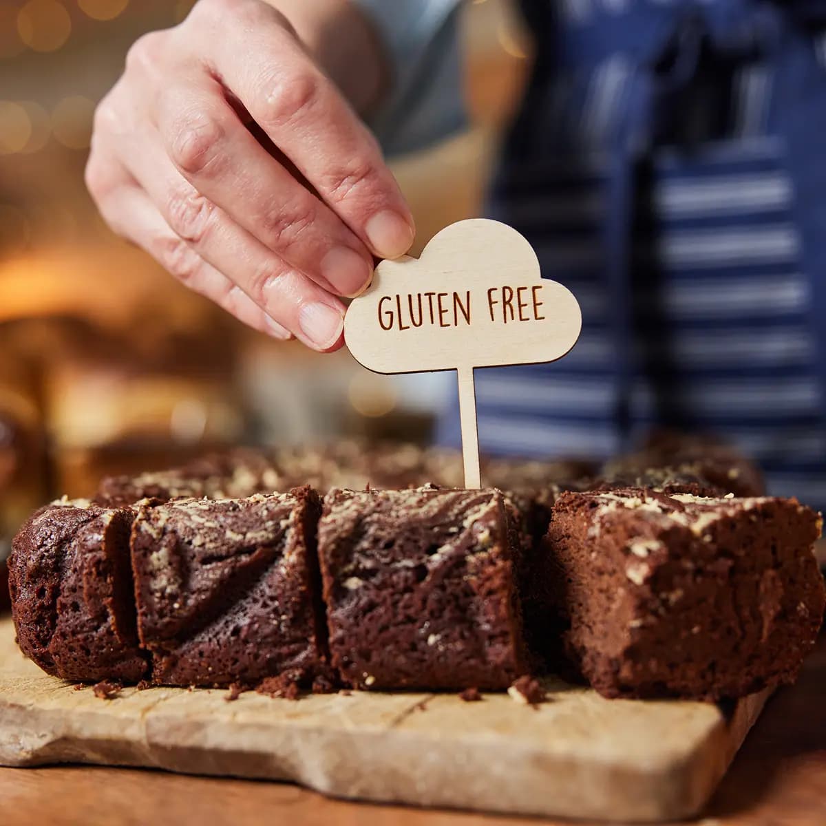 Hand placing a "Gluten Free" sign into sliced chocolate brownies on a wooden serving board.