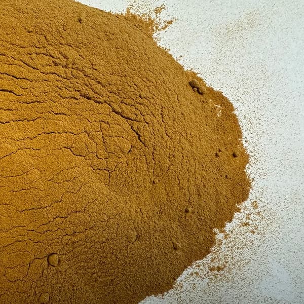 A large pile of finely ground golden-brown almond hull powder spread across a light-colored surface.