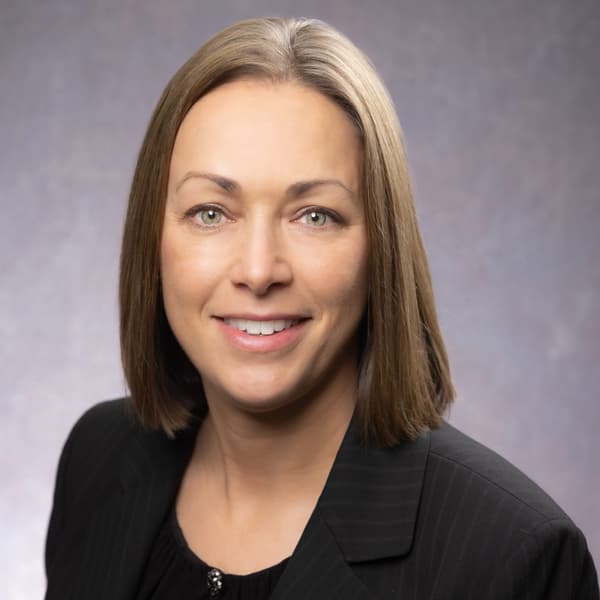Headshot of a smiling woman with shoulder-length hair wearing a black pinstripe blazer.